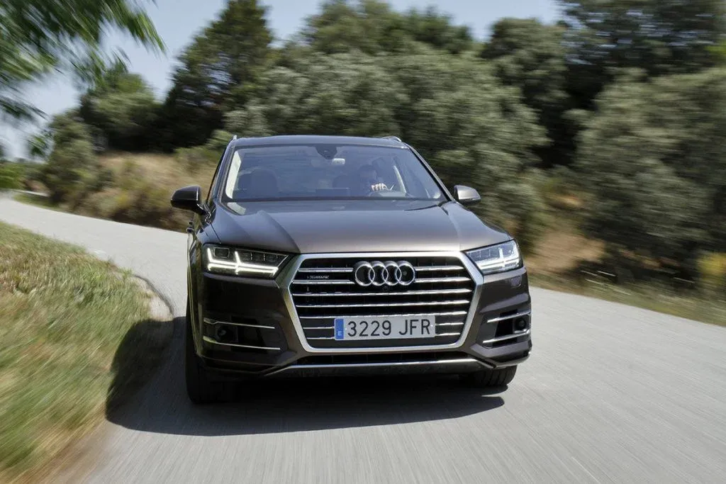 2027 Audi Q7 luxury three-row SUV driving on a paved road with LED headlights on