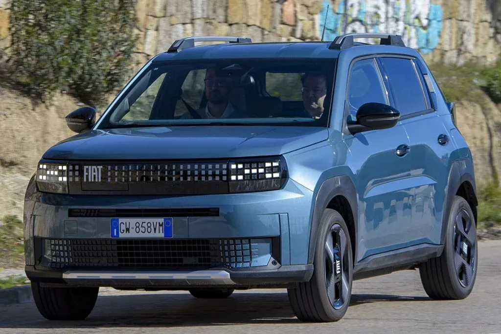 Fiat Grande Panda Hybrid La Prima in heller Lackierung auf einer Stadtstraße, aufgenommen schräg von vorn