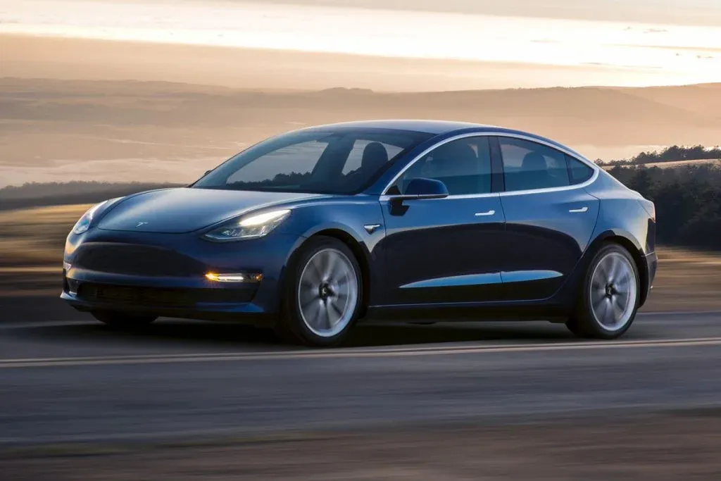 Tesla Model 3 driving through a suburban residential street near homes in daylight